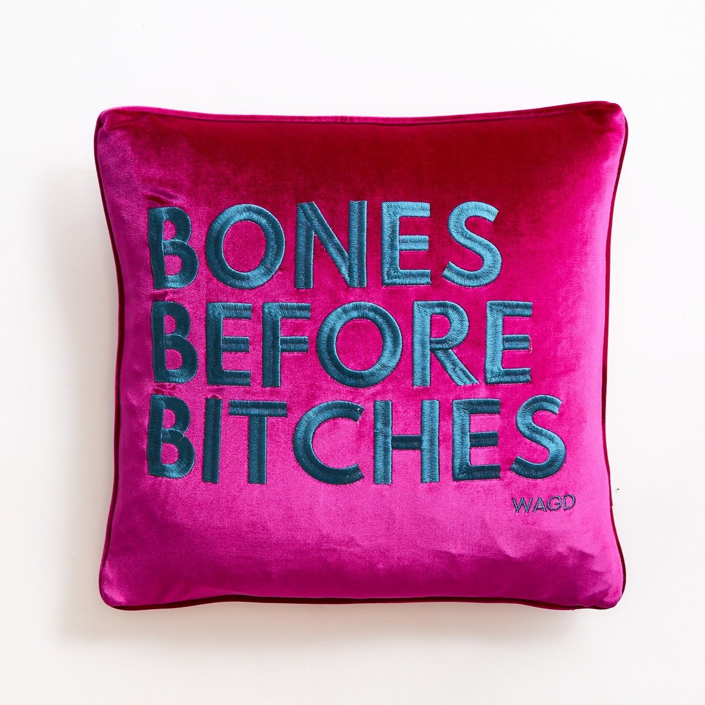 velvet square pillow with Bones Before Bitches embroidered on to it. Bright pink base with peacock embroidery.