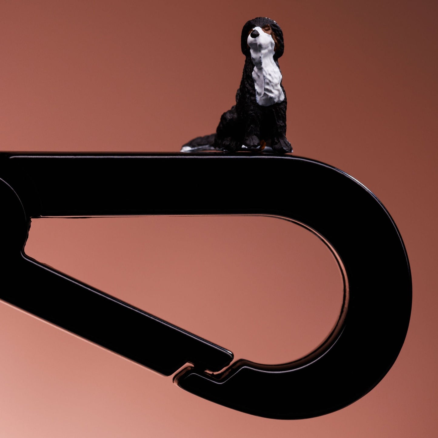 Close up of a black metal dog lead clip. A black and white small model dog is balanced on top.