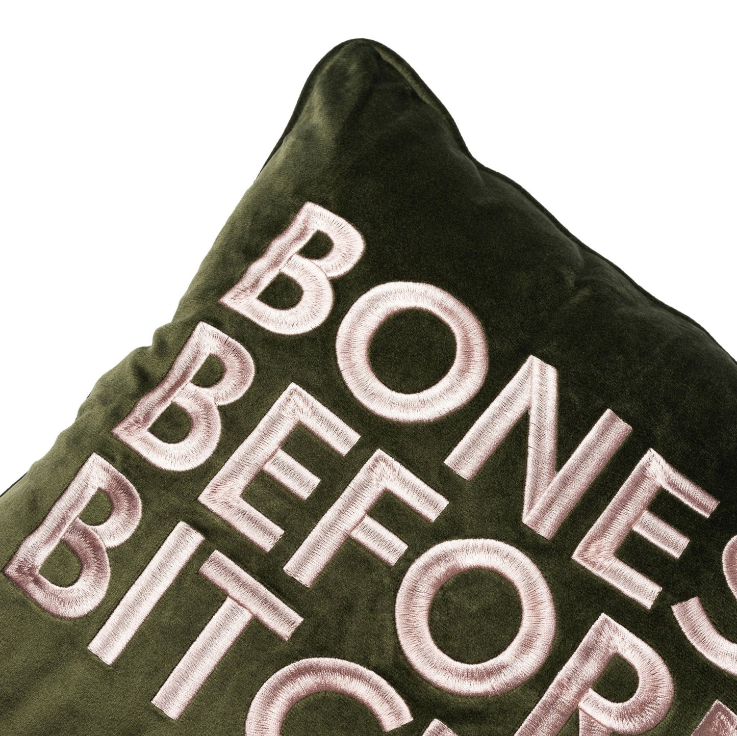 Side view of velvet square pillow with Bones Before Bitches embroidered on to it. Olive base with pink embroidery.