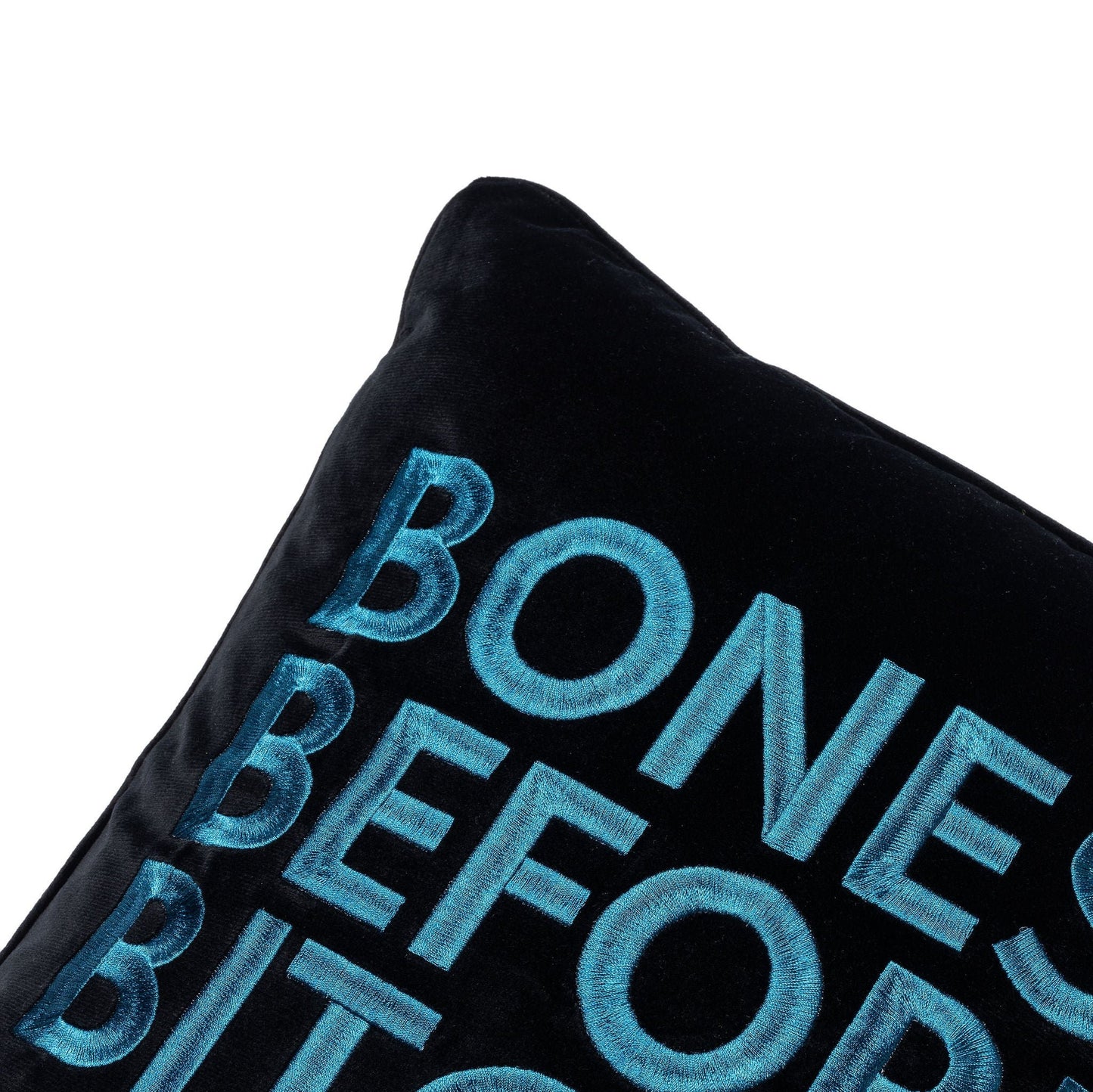 Side view of velvet square pillow with Bones Before Bitches embroidered on to it. Black base with peacock embroidery.