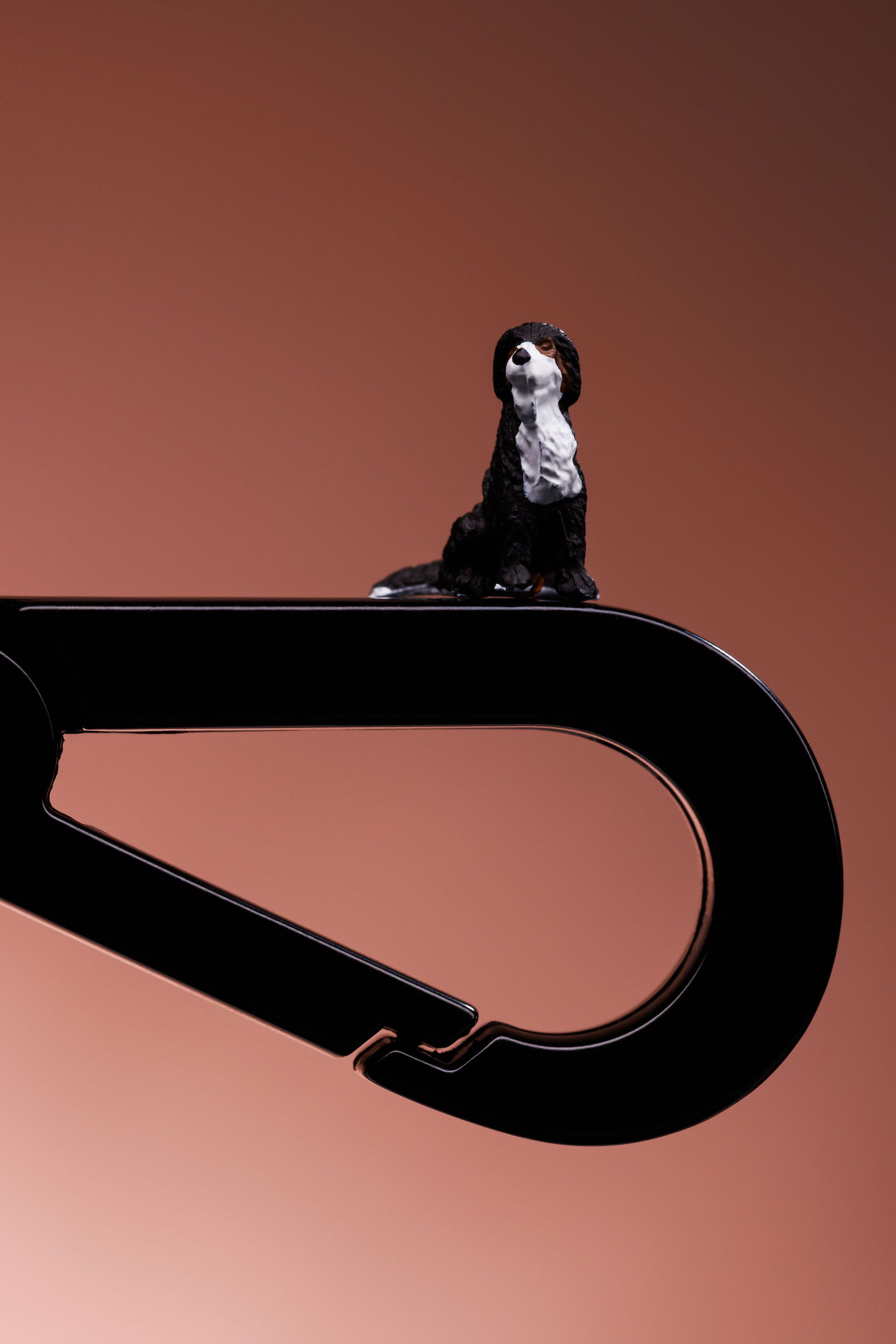 Close up of a black metal dog lead clip. A black and white small model dog is balanced on top. 