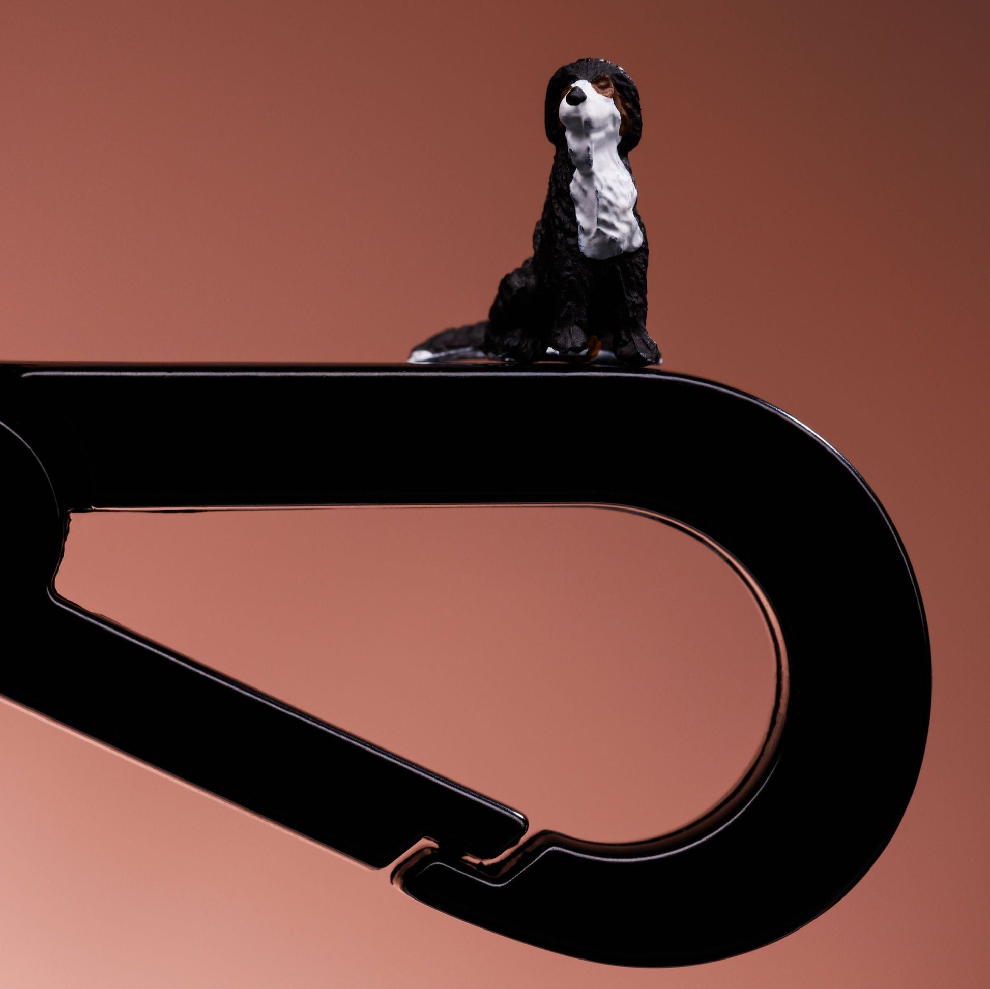 Close up of a black metal dog lead clip. A black and white small model dog is balanced on top. 